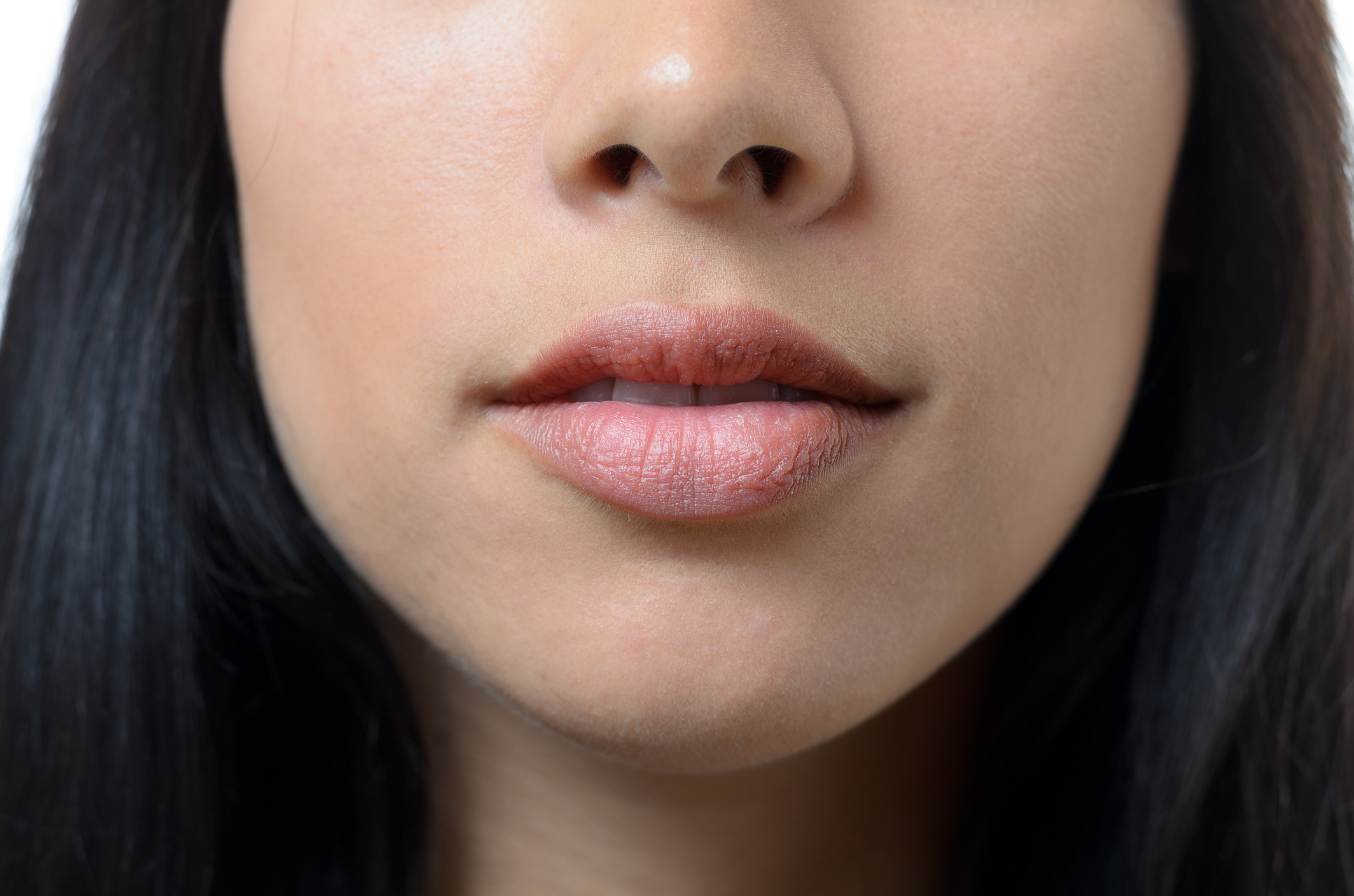 Natural lips and mouth of a young woman with no makeup and long dark hair, close up cropped view of her lower face