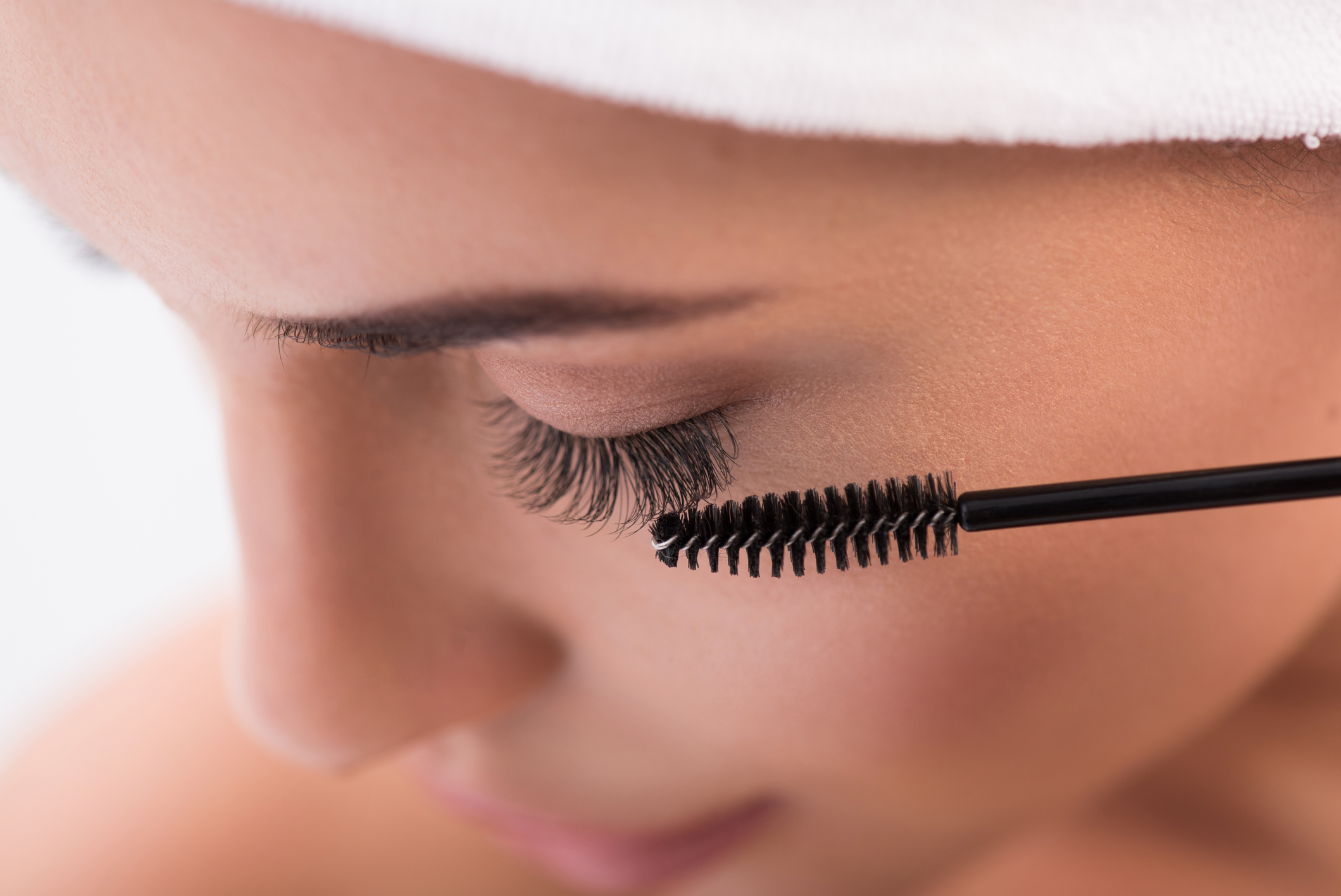 Close up of young calm woman face tightening up her artificial eyelashes by brush